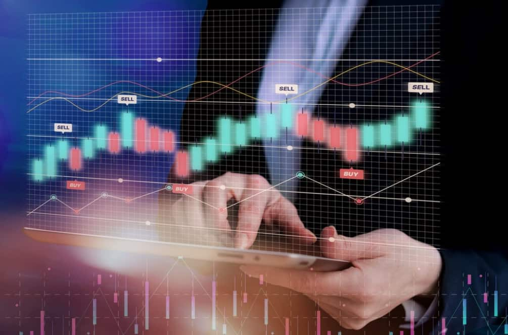 Hands holding a tablet showing stock market buy and sell signals